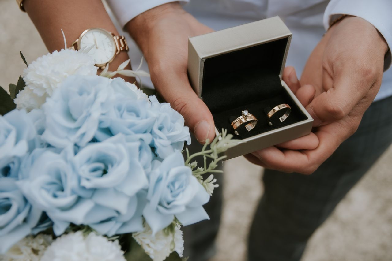 Romantic close-up of wedding rings in a box held with a bouquet of blue flowers, perfect for wedding themes.
